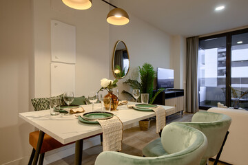 Dining table in living room with glassware and cutlery prepared flanked by designer chairs upholstered in light green velvet