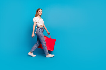 Full length profile portrait of lovely girl hold store bags walk empty space wear top isolated on blue color background
