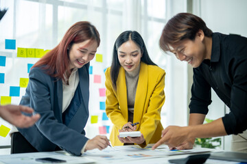 Three people are sitting at a table, one of them is writing on a white board. Scene is collaborative and focused, as the group is working together to come up with ideas or solutions