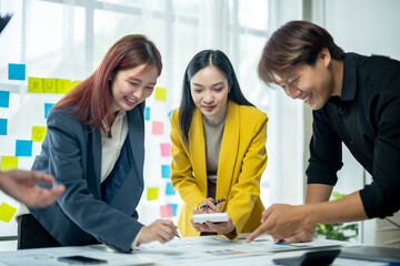 Three people are sitting at a table, one of them is writing on a white board. Scene is...