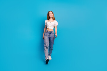 Full size photo of nice young girl look walk empty space wear top isolated on blue color background