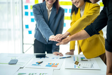 Three people are standing around a table, one of them is wearing a yellow jacket. They are all smiling and shaking hands