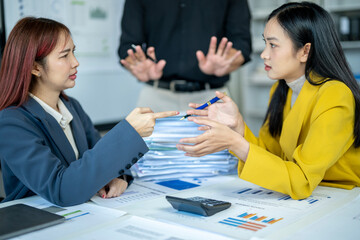 Two women are arguing in a business meeting. One of them points at the other and says