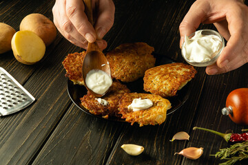 Close-up of a chef hands adding sour cream to fried potato pancakes with a spoon. Concept of...