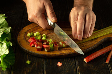 The chef chops fresh rheum plant with a knife on a wooden cutting board. Vegetarian menu for a restaurant or hotel