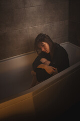 Sad woman sitting with knees drawn up in tub.