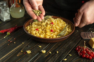 Cooking pasta with spices on the kitchen table. The chef hand adds cardamom to the plate for flavor and aroma.