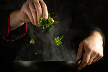An experienced chef adds fresh parsley to a hot pan by hand. The concept of preparing a delicious...
