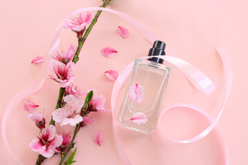 Top view of elegant perfume bottle with cherry tree flowers over pastel pink background. Cosmetics, fragrance and perfumery concept