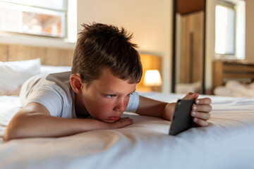 Boy lying on bed with smart phone. The boy is playing games on his smartphone, lying on bed at home.