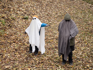 Two boys dressed as ghosts in grey and white sheets, Halloween celebration with brothers in nature,...