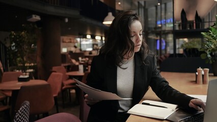Caucasian beautiful girl with dark long hair sitting in the restaurant, looks serious and working...