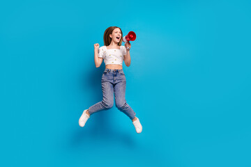 Full size photo of nice young girl loudspeaker jump raise fist wear top isolated on blue color...