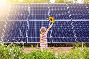 Young 6 year old blonde girl child standing in front of small solar panel farm in countryside....