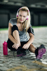 Young woman resting after outdoor workout with headphones and water bottle