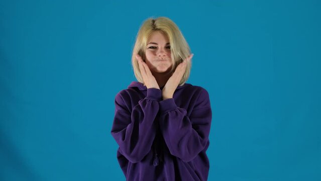 Teenager person taps puffy cheeks grimacing on blue background. Funny short haired woman makes face playing. Silly face expression