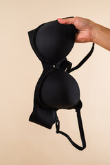 Elegant black bra in female hand isolated on light background