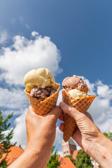 Eistüte mit Eiskugeln in der Hand vor blauem Himmel