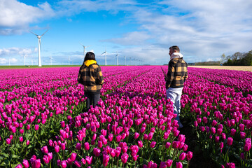 Two people stand amidst a vibrant field of purple tulips in the Dutch countryside, surrounded by...