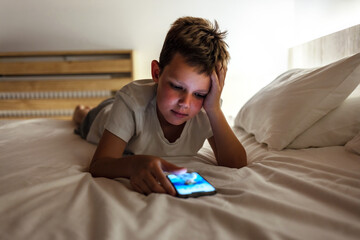 Cute little boy sitting in the dark and watching cartoons on mobile. Boy searching the internet at...