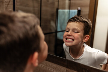 Shot of a little boy checking his teeth in the mirror at home.