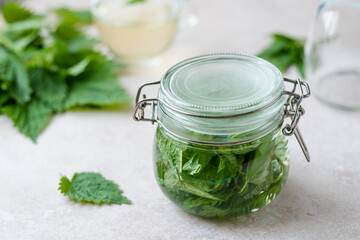 Homemade herbal remedy nettle tincture a in closed glass jar on white table. Weight loss and detox....