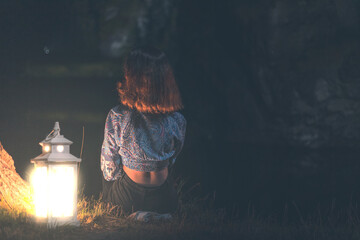 Beautiful girl sitting by the lake at night with a lantern