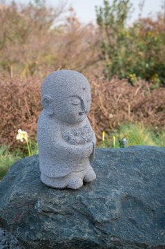 Stone statue of Buddha Jizo with flowers in Japanese garden.