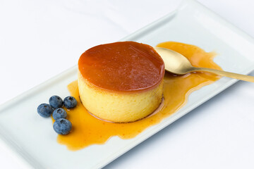 Creme brulee dessert served with syrup and a bunch of blueberries, on a rectangular plate. 