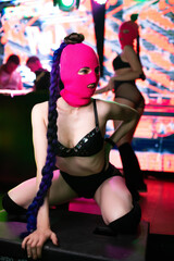 Beautiful girl in black underwear and a pink balaclava posing on the stage of a nightclub. Party concept
