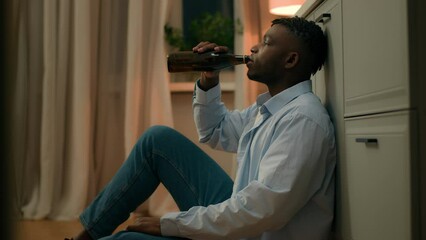 Sad upset African American man drunk male addicted guy alcohol addiction drinking beer alone at home kitchen evening on floor suffer heartbreak divorce health problem alcoholism bankruptcy loan lost