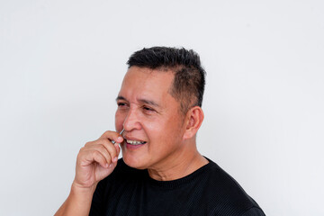 Middle-aged Asian man grooming, removing nose hairs with tweezers on white background