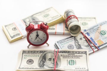 One dollar bills on a wooden table with a red alarm clock in the composition. Money saving concept.