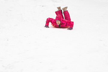 childhood, sledging and season concept - happy little girl sliding down on sled outdoors in winter - obrazy, fototapety, plakaty