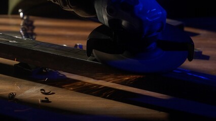 Craftsman in protective gloves and overall working with grinder at industrial plant, man silhouette grinding iron detail on the table in workshop. Close up shot.