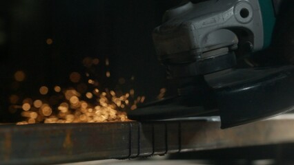 Craftsman in protective gloves working with grinder at industrial plant, man grinding iron detail, sparks flying at the camera.