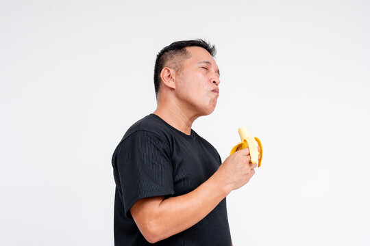 A middle-aged Asian man savoring the sweet taste of a ripe lakatan banana. Isolated on a white background.