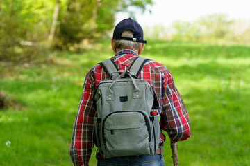 Rear view of senior man with backpack standing in the meadow