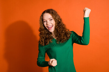 Photo of lucky excited lady dressed green shirt rising fists emtpy space isolated orange color...