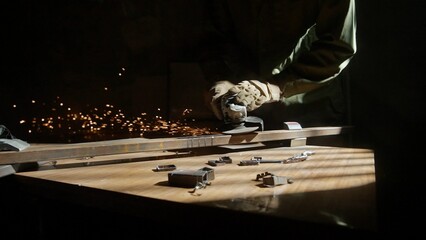 Craftsman in protective gloves and overall working with grinder at industrial plant, man silhouette grinding iron detail on the table in workshop.