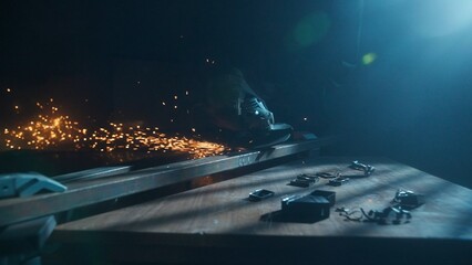 Craftsman in protective gloves and overall working with grinder at industrial plant, man silhouette grinding iron detail on the table in workshop.