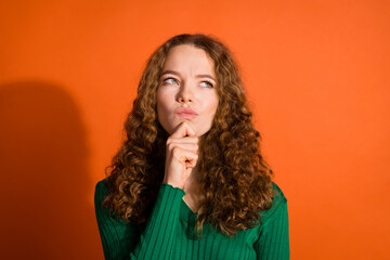 Photo of doubtful unsure lady dressed green shirt hand chin looking emtpy space isolated orange...