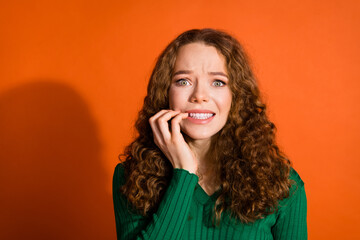 Photo of unsure scared lady dressed green shirt biting fingers emtpy space isolated orange color...