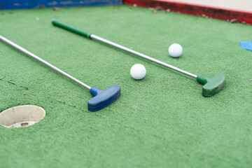 Mini-golf clubs and balls of different colors laid on artificial grass