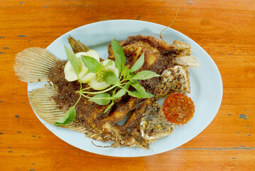 Grilled gourami or gurame bakar with vegetables and indonesian chilli sauce. Serving on wooden table. 