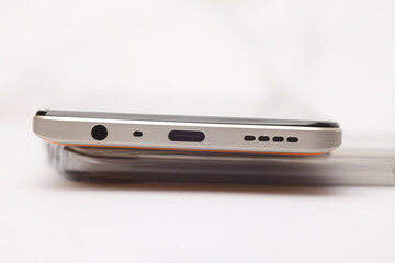 Bottom panel of a modern smartphone with holes for charging, connecting headphones and speakers on a white background