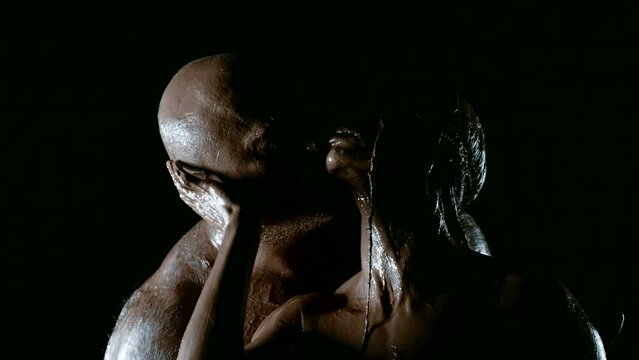 In a gloomy atmosphere, an intimate story of passion and affection blossoms on a black background, where a man with a strong physique and his gorgeous wife, entwined with clay, meet in an embrace