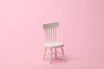 White mirniature chair on a pink background. Minimalism.
