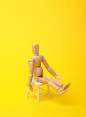 Wooden puppet sitting on a chair, yellow background