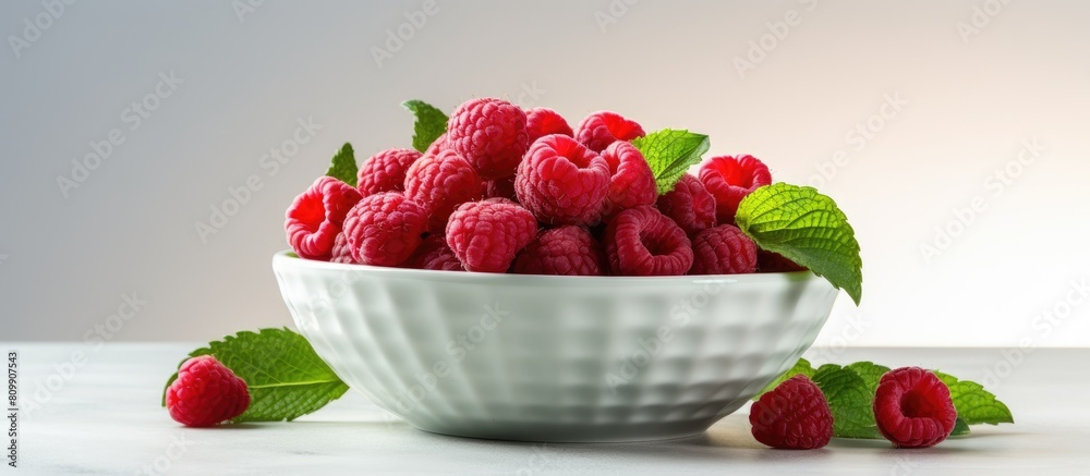 Poster a closeup copy space image of a bowl containing fresh raspberries and mint leaves placed on a light 